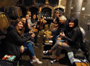 A group of people in the premises of a wine cellar tasting wine blind