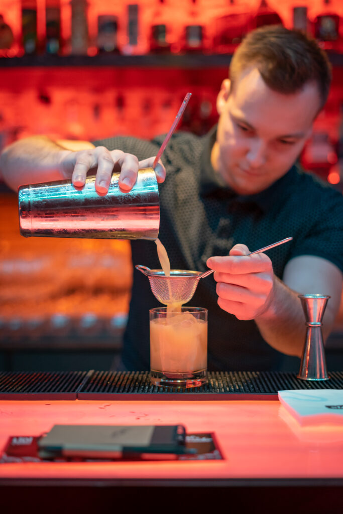 Bartender pouring drink through strainer
