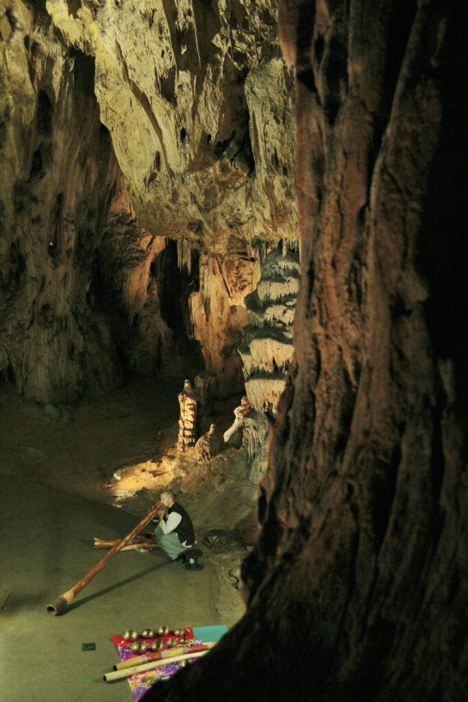 A musician with a didgeridoo producing music in a cave