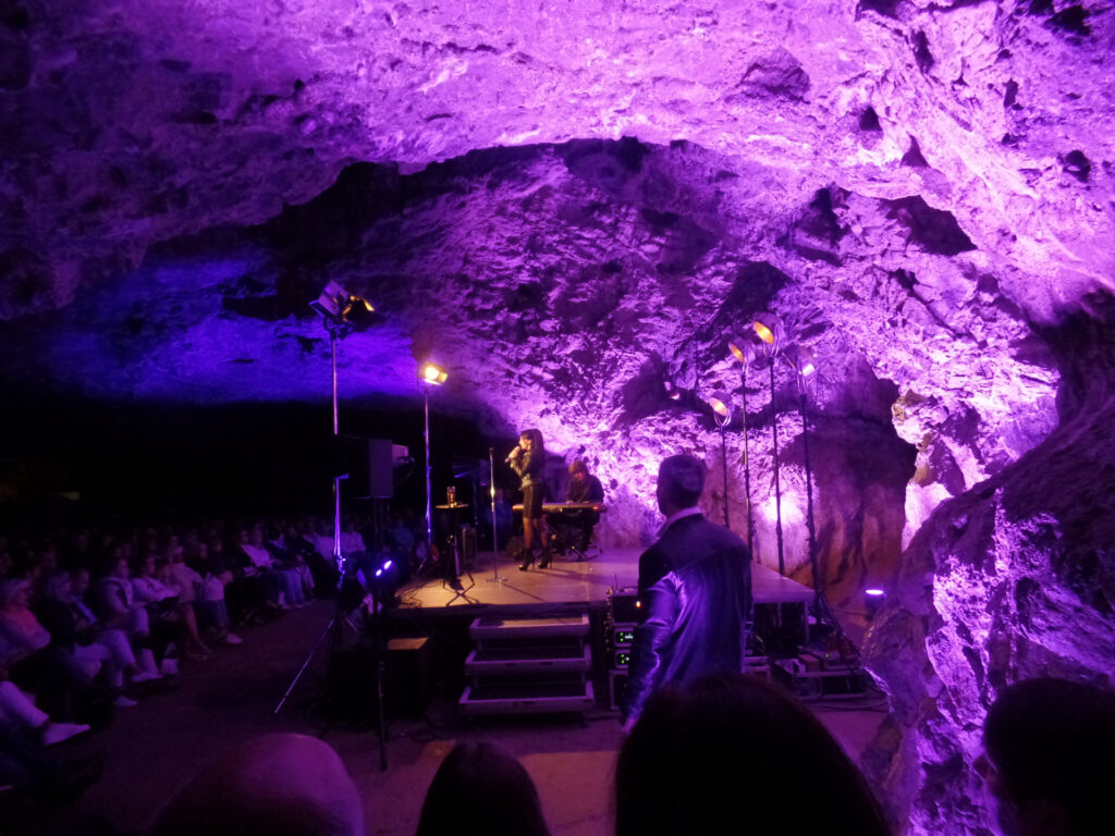 A concert in a cave with a purple-lit stage and a musician