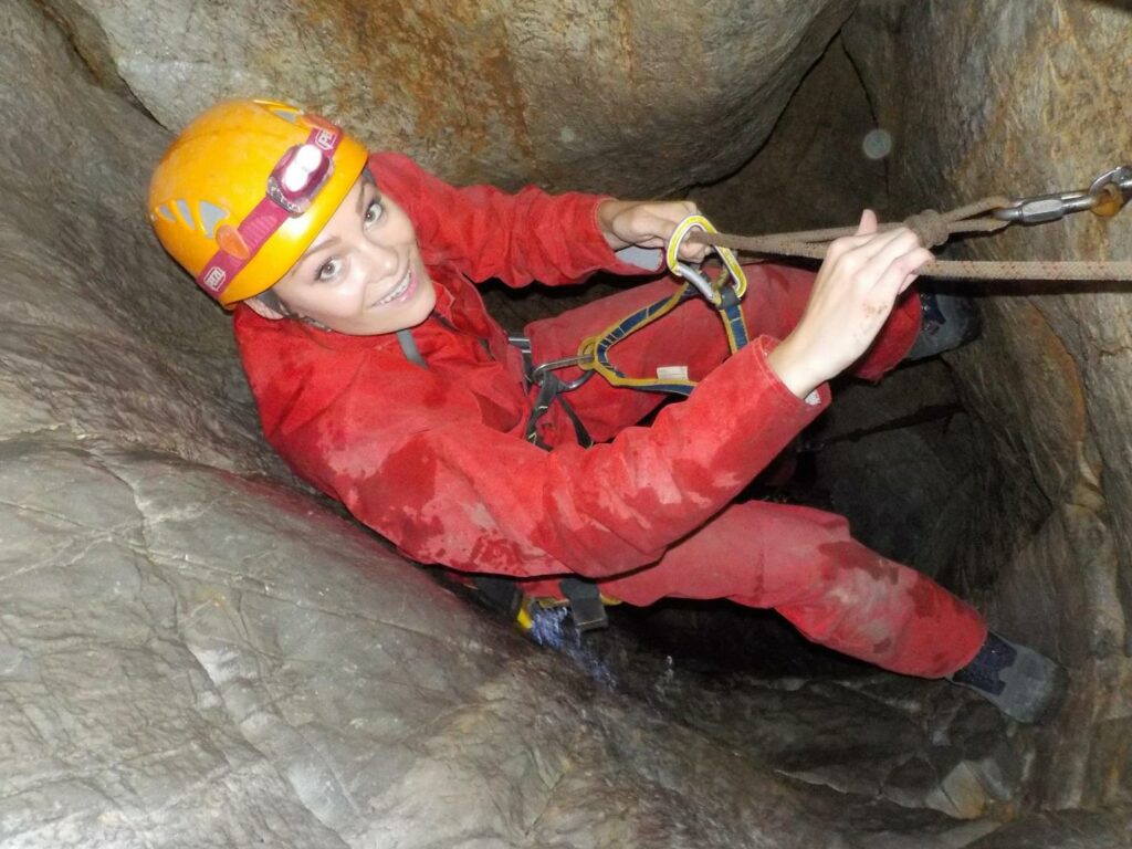 A lady in overalls abseiling down into the bowels of a cave on a speleofera
