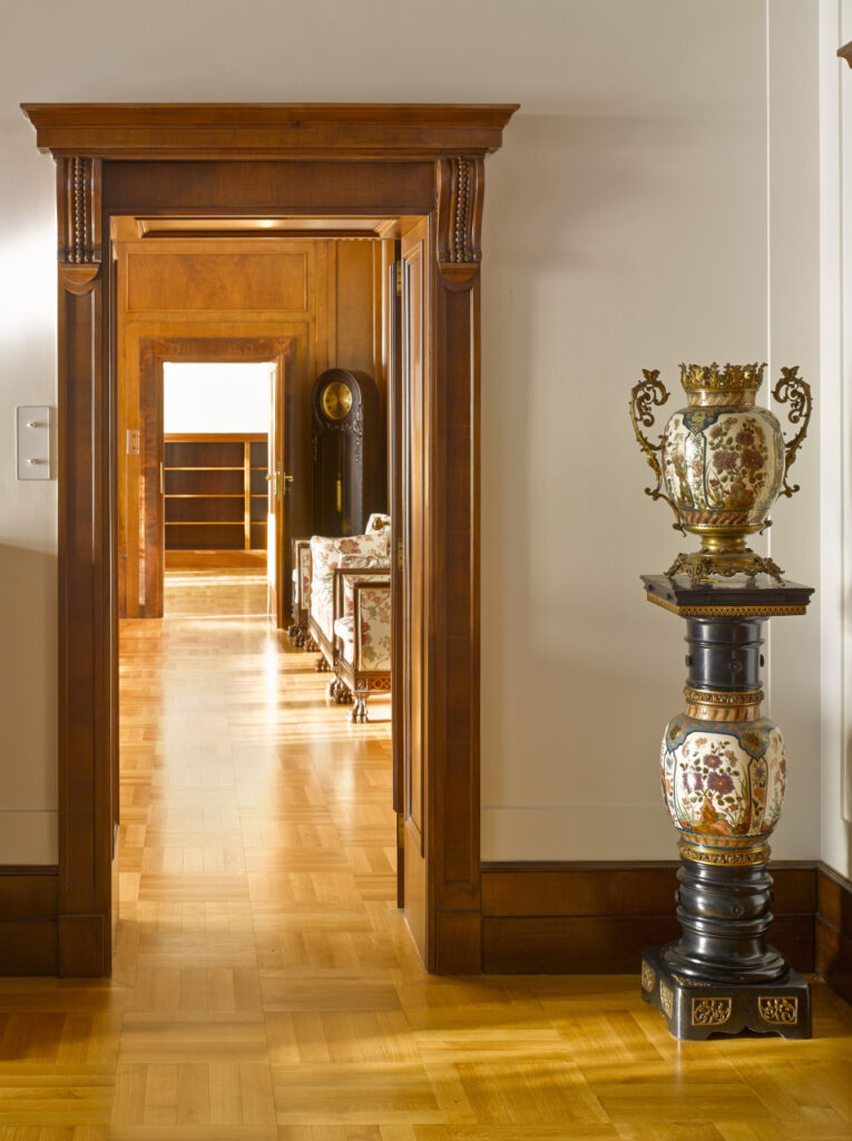 The interior of Villa Stiassni with a view to the door next to which stands a vase on a decorative plinth
