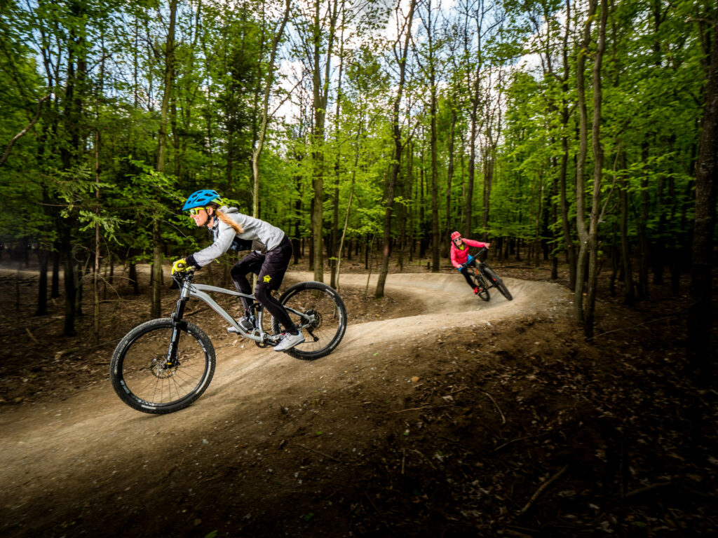 Two female cyclists riding a single trail in the middle of the forest in summer