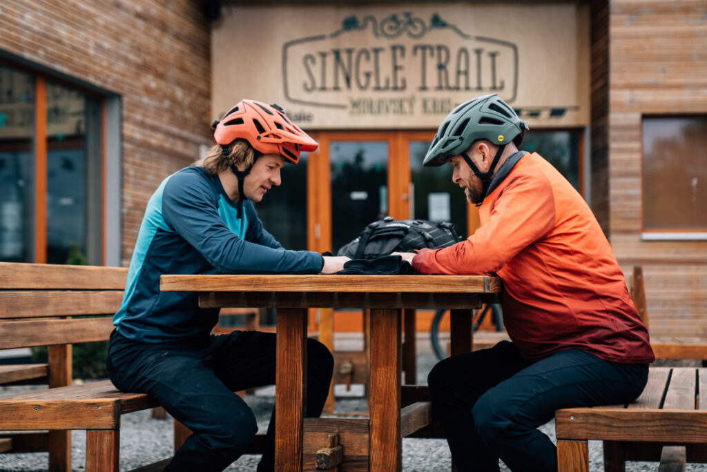 Two cyclists sit on benches in front of the Single Trail Moravsky Karst