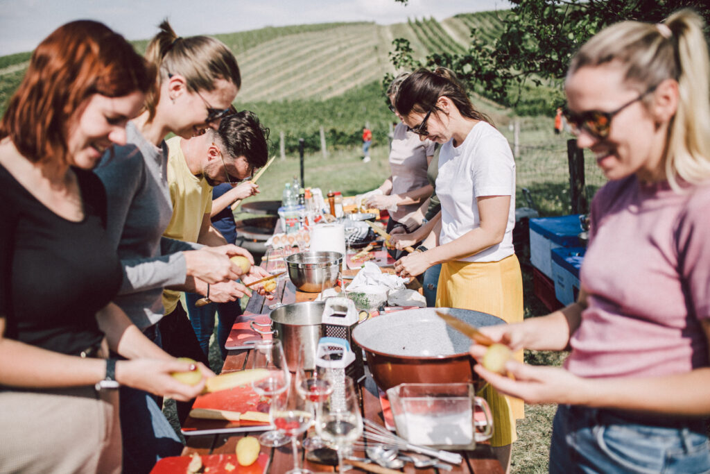 A group of people cook at one table in the middle of a vineyard