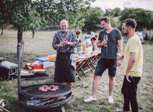 Three people standing at a grill where hamburgers are being fried