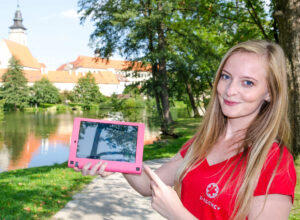 a lady in a red t-shirt holding a pink tablet in one hand and pointing at it with the other hand