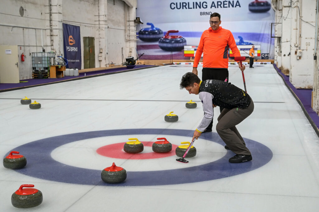 Two people at the end of the curling rink, trying to end the game